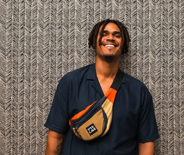 Kam smiling against a black-and-white patterned wall